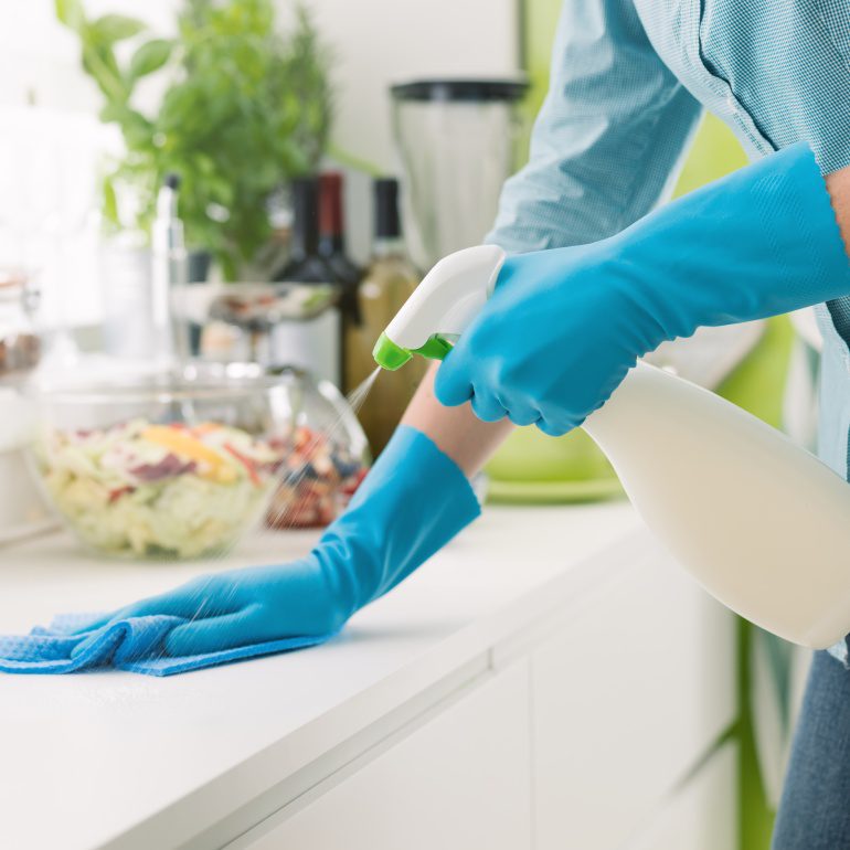 Person cleaning counter with spray bottle.