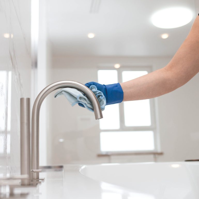 Person cleaning a chrome faucet with a cloth.