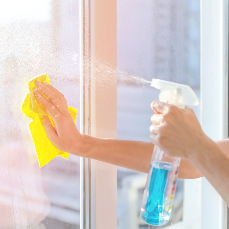 Cleaning window with spray bottle and cloth.